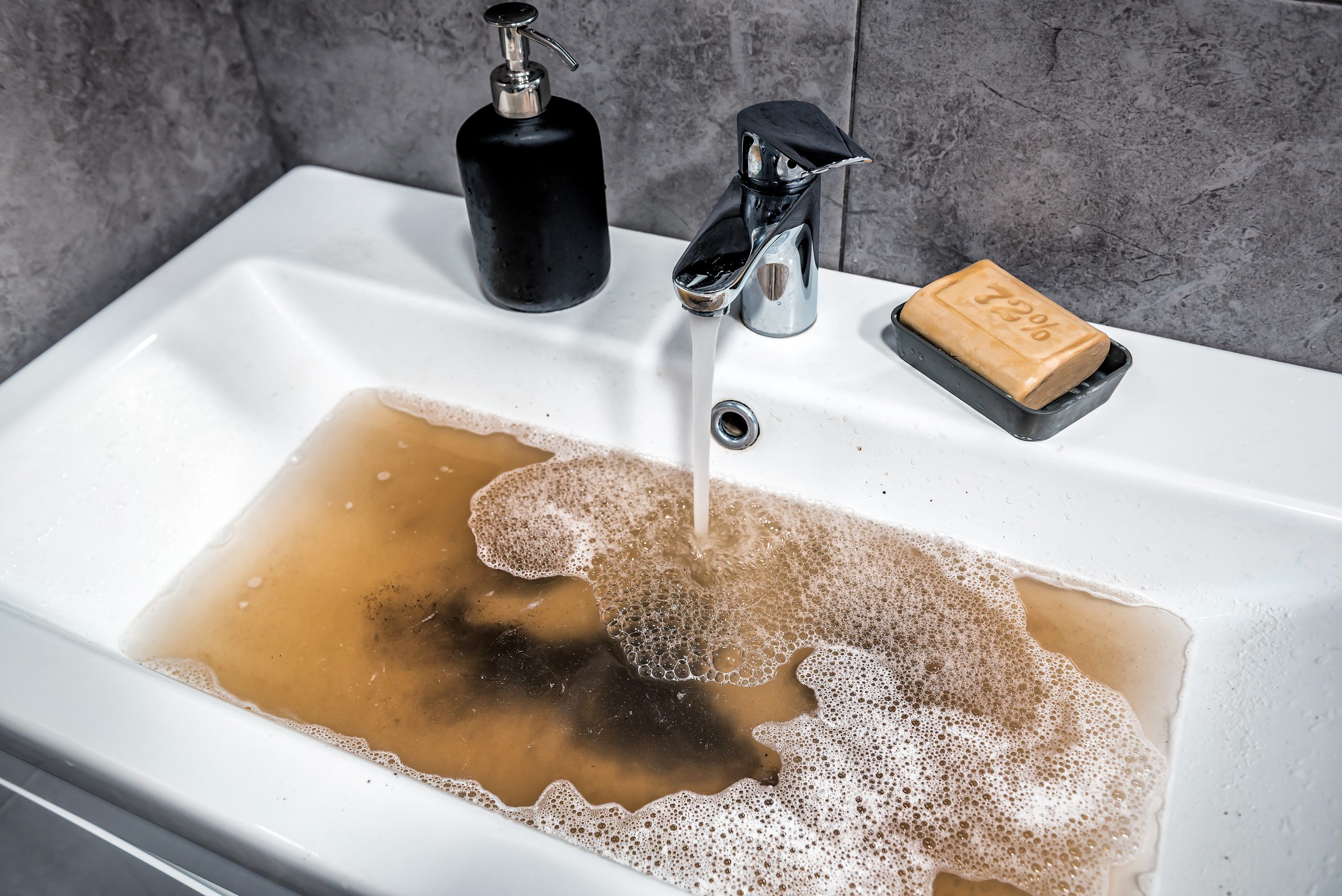 Clogged bathroom sink being repaired with professional drain clearing tools.